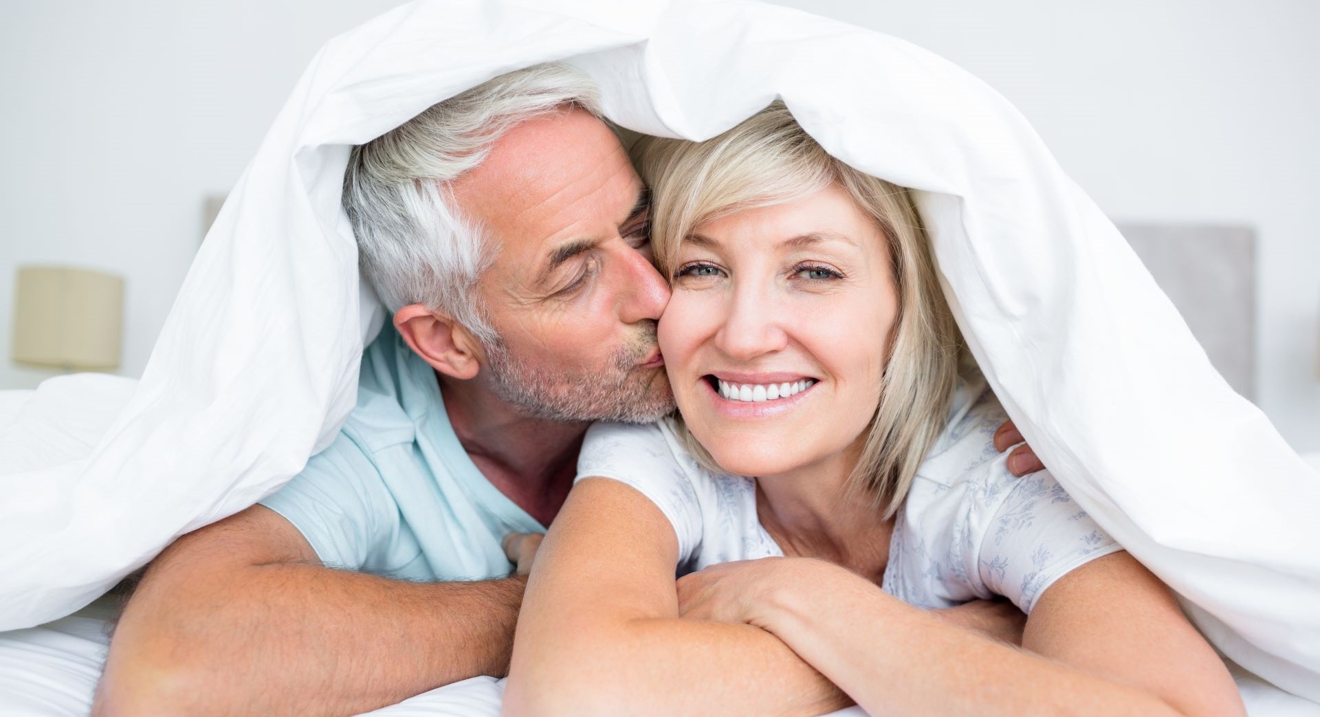 Man laying in bed and kissing smiling woman next to him on the cheek