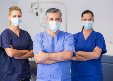 Three smiling dental team members in scrubs and face masks