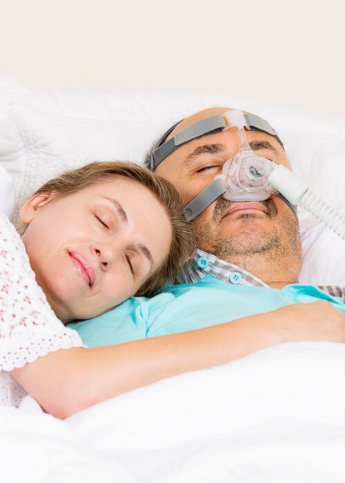 Man with obstructive sleep apnea wearing C P A P mask while sleeping next to woman