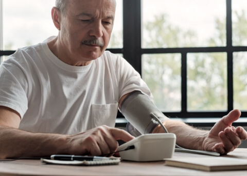 Man at his kitchen table using a blood pressure reader