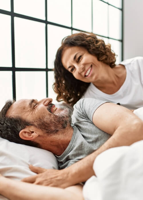 Man and woman smiling at each other in bed after sleep apnea services in Cumming