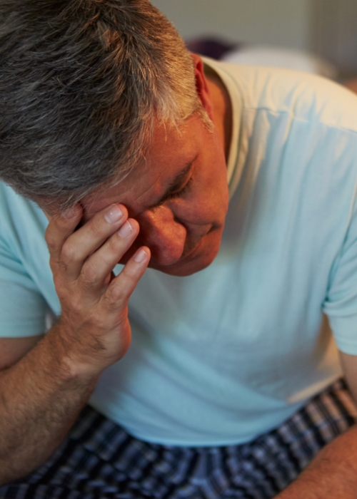 Man with sleep apnea sitting up in bed and pinching the bridge of his nose