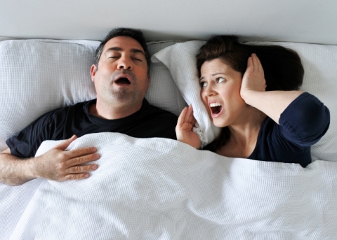 Woman in bed covering her ears next to snoring man