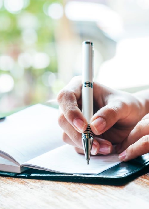 Person writing in a small notebook with a pen