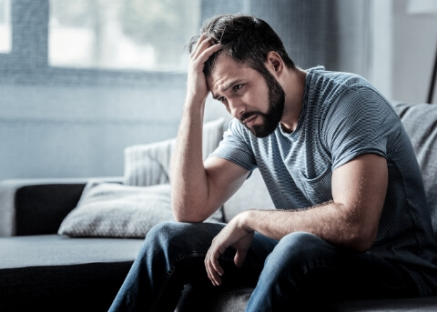 Frustrated man sitting on edge of bed and running his hand through his hair